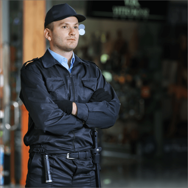 Uomo in uniforme di sicurezza con braccia incrociate e una torcia, in ambiente interno.