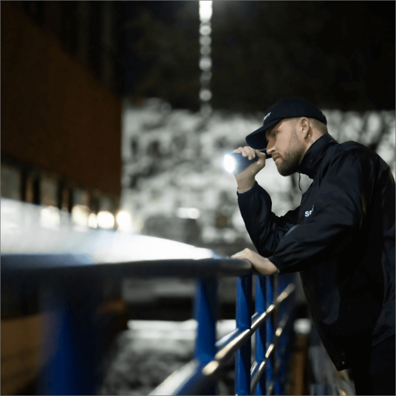 Uomo con torcia, appoggiato a un parapetto in un ambiente notturno.